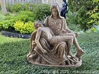 Full view of the Virgin Mary holding Jesus statue surrounded by garden greenery to show its use as garden decor.