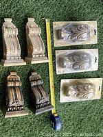 Front view of two gold-tone and two dark-tone decorative wall sconces arranged with a measuring tape.