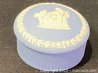 Top and angled view of the round Wedgwood blue jasperware trinket box showing the white relief classical figures on lid and leaf wreath border