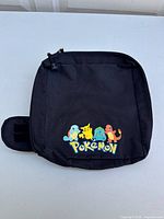 Front view of the black crossbody bag with colorful 90's Pokemon character prints of Squirtle, Pikachu, Bulbasaur, and Charmander above the Pokemon logo.