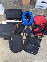 Top view of all 7 assorted bags laid on ground showing various sizes and colors including black, blue, gray, and red bags.