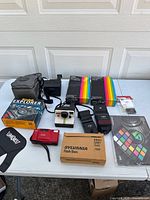 Wide view of entire camera lot showing multiple cameras, flashes, film packs, and accessories on table