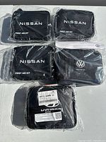 Photo of five black nylon first aid kits in plastic wrap, three Nissan, one Volkswagen and one Hyundai.
