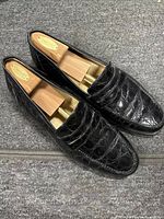 Pair of black crocodile embossed leather loafer dress shoes size 13 M with wooden shoe trees inserted, top view.