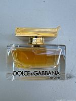 Front view of partially full Dolce & Gabbana The One perfume bottle with gold cap and amber liquid inside.