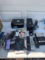 Overview of electronics lot with printer, barcode scanner, remote controls and boxed amplifier