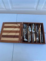 Wooden box open showing multiple compartments holding assorted flatware pieces.