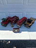 Five wooden vintage-style vehicles arranged on a white table under sunlight showing overall condition and lot contents.