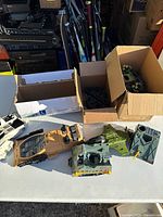 Seven GI Joe vehicle parts including a tan tank body, green angular missile launcher, and white rocket launcher piece, shown on table next to boxes.