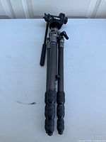 Full view of folded tripod showing carbon fiber legs and handle attached to the head