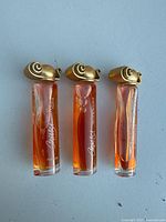 Top angled view of the three Givenchy Paris Organza parfum bottles showing partial fill levels and detail of gold caps with swirl design.