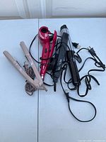 Full view of all hair care tools including Vidal Sassoon flat iron, red hair dryer, and two curling irons showing their cords and plugs