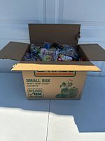 Open cardboard box filled with assorted sealed fast food promotional toys and collectibles.