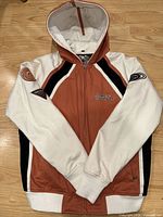 Front view of the hooded Harley Davidson jacket showing color blocks of orange, white, and black with Harley Davidson embroidery on front and patches on sleeves.