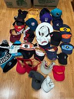 Multiple hats and beanies laid out on wooden floor showing a variety of styles, colors, and brands including USC, Coca-Cola, San Francisco Giants, Sharks.