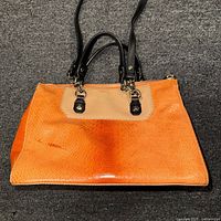 Front view of orange alligator embossed leather tote handbag with beige leather bottom and black leather handles
