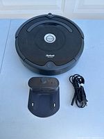 Top-down view showing iRobot Roomba vacuum, charging dock, and power cord together on a surface.