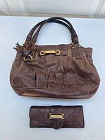 Large brown leather Juicy Couture handbag with top handles and a matching wallet shown together on a surface.