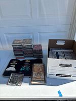 Overview of various CD jewel cases stacked, loose CDs in organizer, Earth, Wind & Fire music album, and Bankers Box with media cases inside.