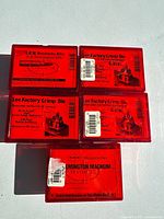 Top view of five red plastic cases of Lee factory crimp dies and reloading dies arranged on a light surface showing label details