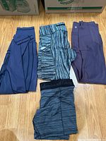Four pairs of folded Lululemon pants laid flat on wood floor showing color and styles.