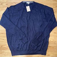 Navy Peter Millar pullover sweater laid flat on wooden floor, showing full front view.