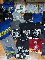 Clothing items with various sports team logos laid out on floor