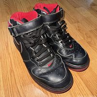 Front and top view of the pair of black and red Nike Air Force One Mid sneakers, showing leather material and lace details.