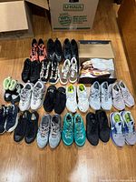 Overview of shoe lot arranged on floor, showing multiple pairs of athletic shoes of various brands and colors.