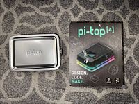 Closed metal carrying case next to the pi-top[4] kit box showing exterior packaging and branding.