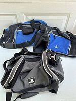 Three Sony PlayStation branded fabric bags visible on the floor, two blue with black trim and one gray and black with white accents.