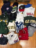 Photo showing overall layout of mixed clothing lot with hoodies, jerseys, shirts, and caps in various colors and logos