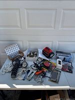 Photo showing an assortment of tools including stapler, tape measure, flashlight, pliers, and cords on a table.