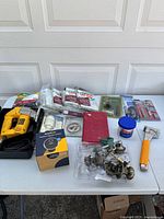 Full view of all tools and hardware on a table including jigsaw, door knobs, nails, light bulb, sanding disk, mallet, and putty knife.