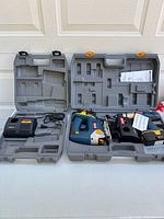Two open gray carrying cases, one holding cordless jigsaw and battery, the other holding battery charger with power cord
