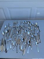 Large collection of mixed silverware and flatware pieces including forks, spoons, knives, and serving utensils with various handle styles.
