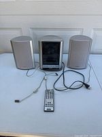 Front view of Sony CMT-EX5 central unit flanked by two matching satellite speakers with remote control in front. Shows overall system and cables.