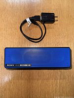 Blue Sony SRS-X33 Bluetooth speaker and black AC-UUD11 charger with cable on wooden surface