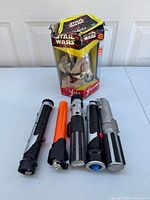 Photo of the interactive Yoda figure in original packaging along with four Star Wars lightsabers laid out for display.