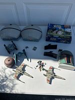 Top down view of lot showing two large gray vehicle bases with orange details, two X-Wing starfighters with red markings and two small TIE fighters, a brown speeder/droid, several small figure pieces, a Boba Fett helmet/display.