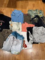 Overview of lot with folded Tommy Bahama shirts and assorted garments on wooden floor, showing different colors and prints including blue, floral, coral, and black items.