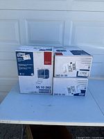 Three boxed Tork Matic Hand Towel Dispensers, model 55 10 282, stacked on a surface in front of a white garage door.