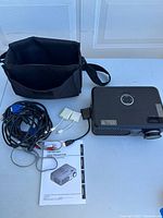 Full lot contents including projector, cables, remote, manual, and carrying bag laid out on table.