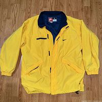 Full front view of yellow windbreaker jacket with zippered pockets and Nike swoosh on chest.