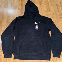 Front view of black hoodie showing minimalist front design with stylized Nike skull swoosh and NBA skeleton logo.