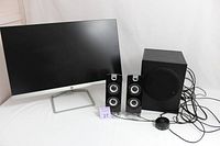 Photo of HP 24.8-inch computer monitor with PA CA3602 speaker set including two satellite speakers and one subwoofer with wired control knob and connecting cables, all placed on white surface.