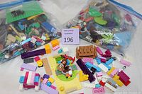 Overview of three large plastic bags of assorted used LEGO parts and many LEGO pieces spread out on a white surface including baseplates, bricks, and figurines.