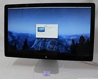 Front of Apple Thunderbolt Display showing the full monitor powered on with macOS Yosemite desktop background and display preferences window.