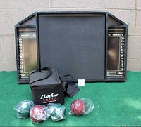 Viper dart back board standing against a wall with Baden bocce balls and carrying bag in front, showing full contents and condition.