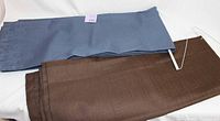 Two curtain panels folded and laid flat, one blue and one brown, showing fabric texture and rod pocket design.